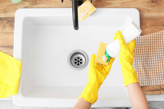 A person in bright yellow gloves just beginning to clean a ceramic sink.