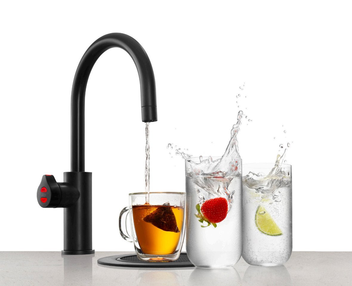 Matte black boiling water tap filling a glass mug with a tea bag.